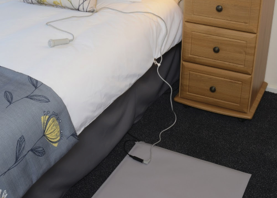 A bed with an electric blanket on it. The cord is loose, which could cause a fall.